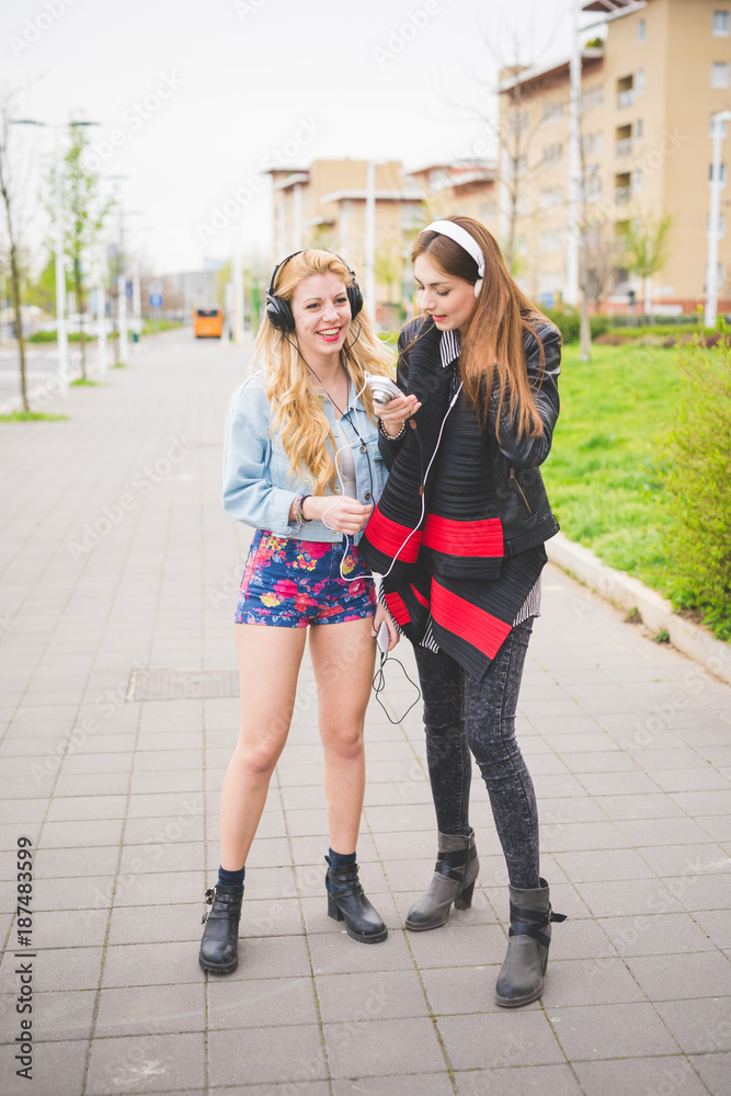 Two young blonde and brunette girls listening to music in the city