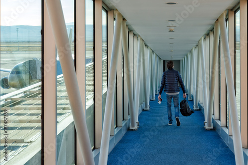 Wallpaper Mural A man with a backpack in his hands walks down the corridor to board the plane. Out the window feed part of the aircraft. Torontodigital.ca