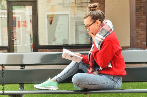 Asian girl sits on a bench and reads a book