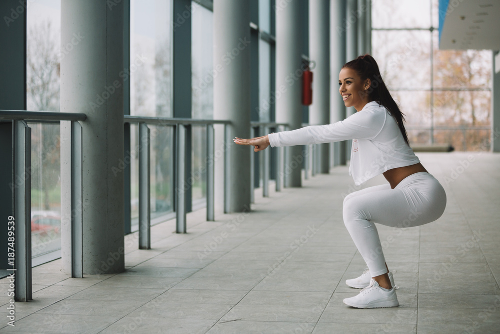 Young fit sporty girl dressed in white doing squat. Young fit sporty girl dressed in white doing squat.