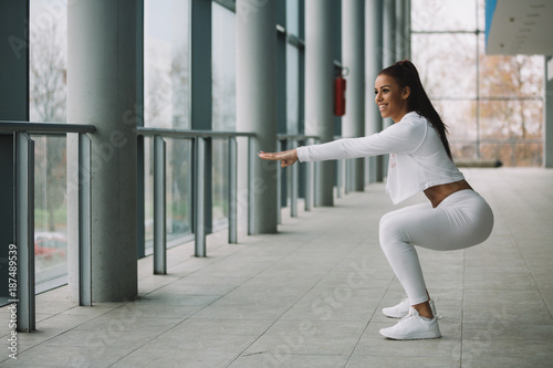 Young fit sporty girl dressed in white doing squat.