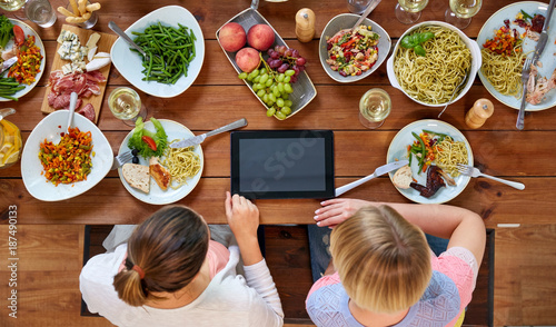 women with tablet pc at table full of food