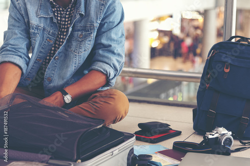 Young man traveler sitting on the floor at the airport terminal finding some stuff, or lost something.  Sad man lost something while travelling aboard.
