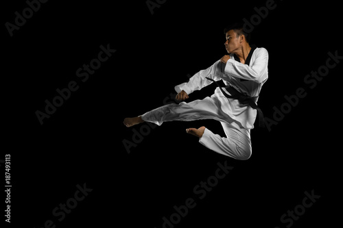Portrait of an asian professional taekwondo black belt degree (Dan) jumping for kick. Isolated full length on black background with copy space