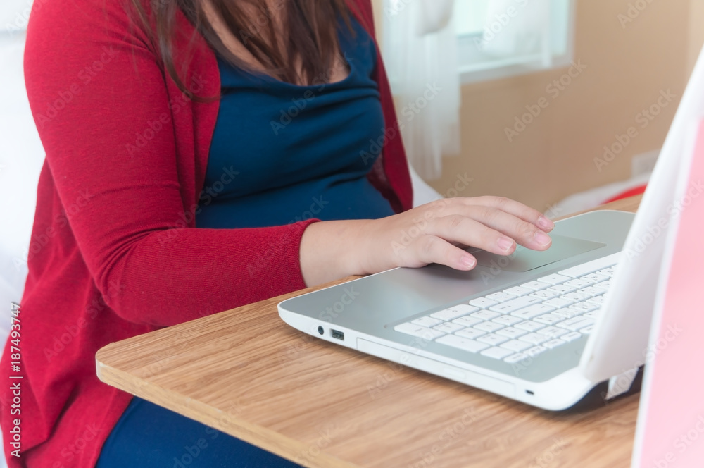 Fototapeta premium Asian pregnant woman wearing red cardigan using laptop and credit card for shopping online website on wooden table and many shopping bag