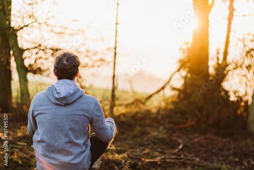 Young man meditating at sunrise in a forrest in Austria