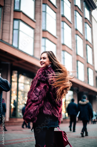 Closeup portrait of glamorous woman with long hair smiling at camera outdoors against the building. She wears black clothes, fashionable sunglasses