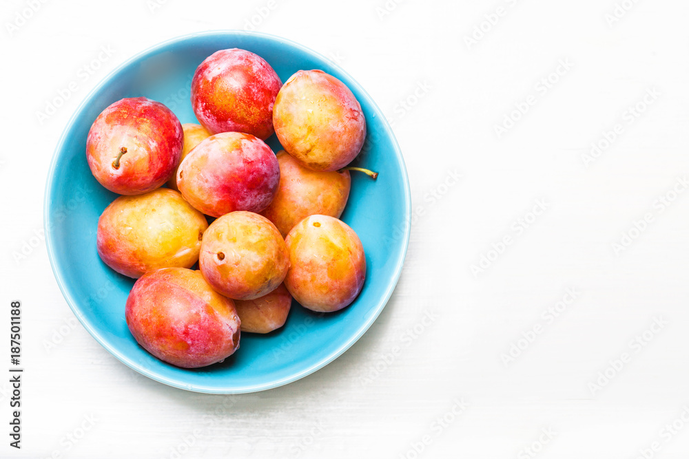 Fresh red cherry plums on white wooden background in a blue bowl with copy space Fresh red cherry plums on white wooden background in a blue bowl with copy space