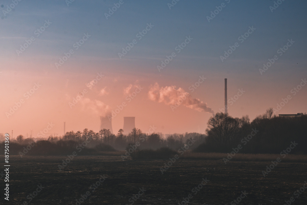 Landscape with field and trees, in the distance factory and a power station, with the factory pipes going smoke against the red sky, Severe pollution of the environment