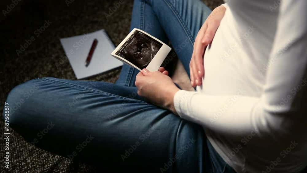 Pregnant woman expecting newborn, holding ultrasound and rubbing belly