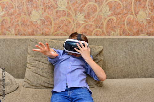 Happy teen boy wearing virtual reality goggles watching movies or playing video games. Cheerful smiling looking in VR glasses and making thumb up gesture. Child experiencing virtual reality. photo