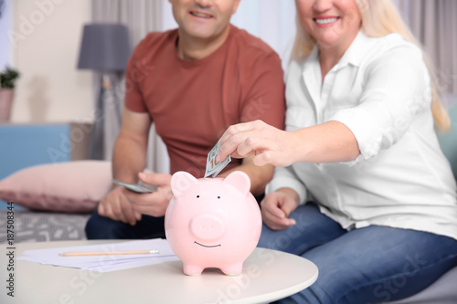 Mature couple putting money into piggy bank at home