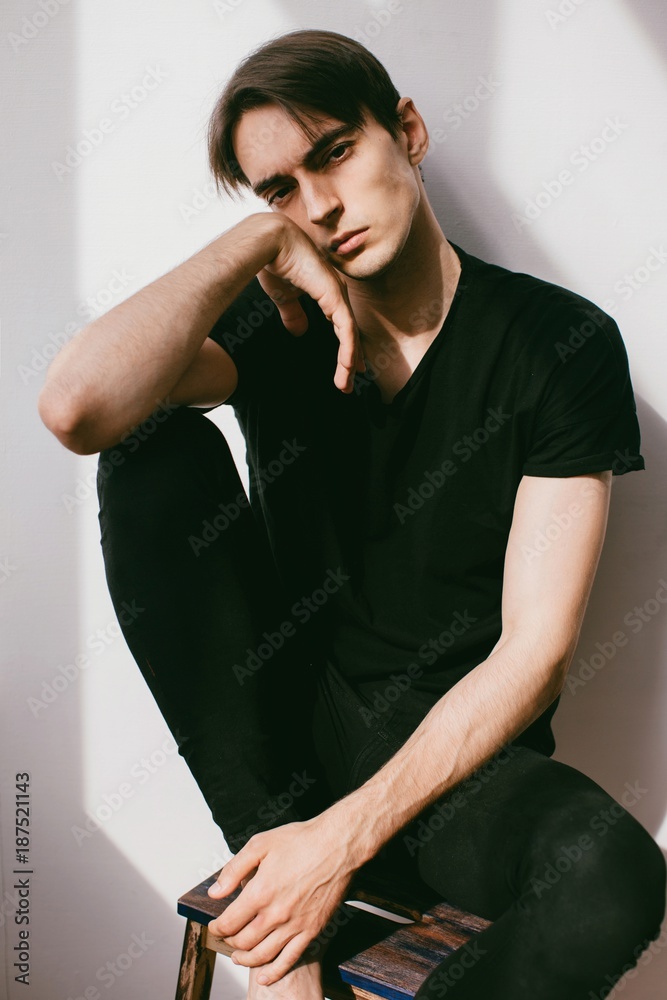 Vertical portrait of young handsome brunet in contrast lightning  and his shadow on white wall