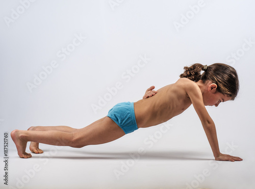 Cute boy in swimming trunks doing gymnastic exercises. Gray background.