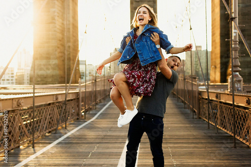 Beautiful young man and woman pose on the Brooklyn Bridge in the rays of morning sun