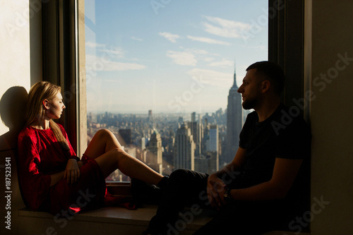 Man and woman sit together on the windowsill with a great cityscape of New York behind them