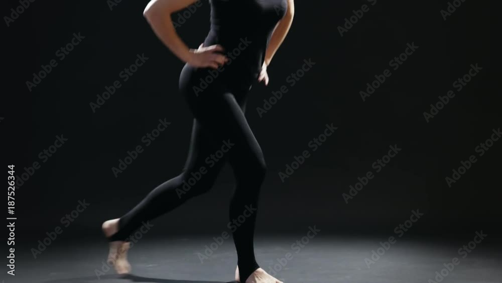 An educative view of a fitness instructor who does back lunges being dressed in a black sportive suit. She does it professionaly in a black gym. An educative view of a fitness instructor who does back lunges being dressed in a black sportive suit. She does it professionaly in a black gym.