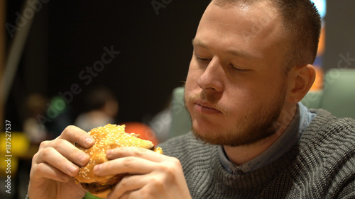 young hipster guy eating burger sitting in cafe