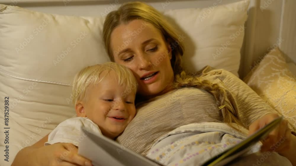 mother and baby son reading a book in bed mother and baby son reading a book in bed