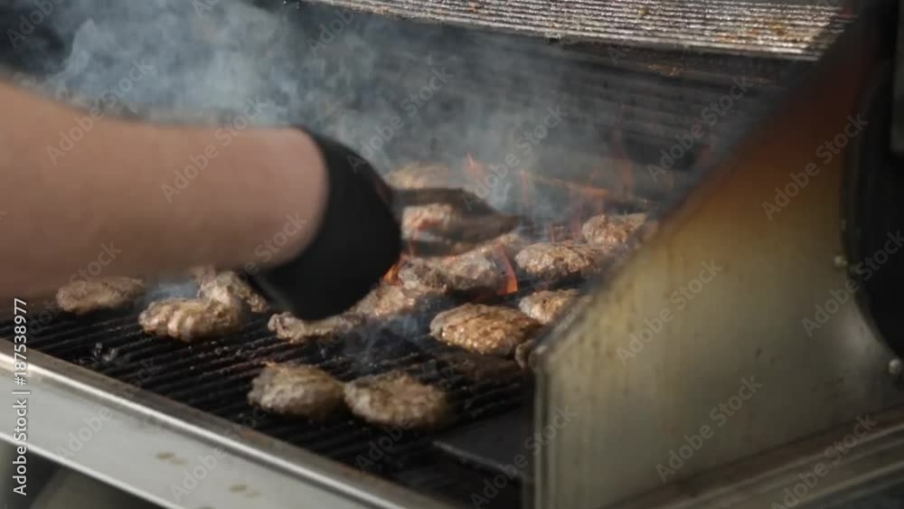 Summertime man cooking food while flipping kosher meat burgers on the grill in outdoors 