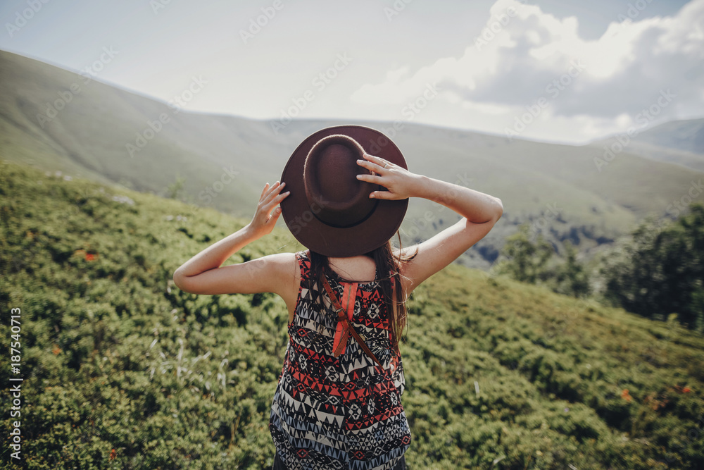 wanderlust and travel concept. stylish traveler woman in hat looking at mountains. hipster girl traveling on top of mountain, raising hands. space for text. atmospheric moment