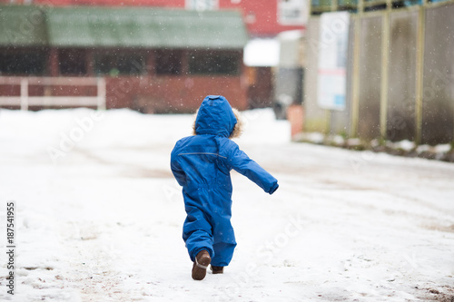 A little boy wearing a blue romper walking by the stable winter time