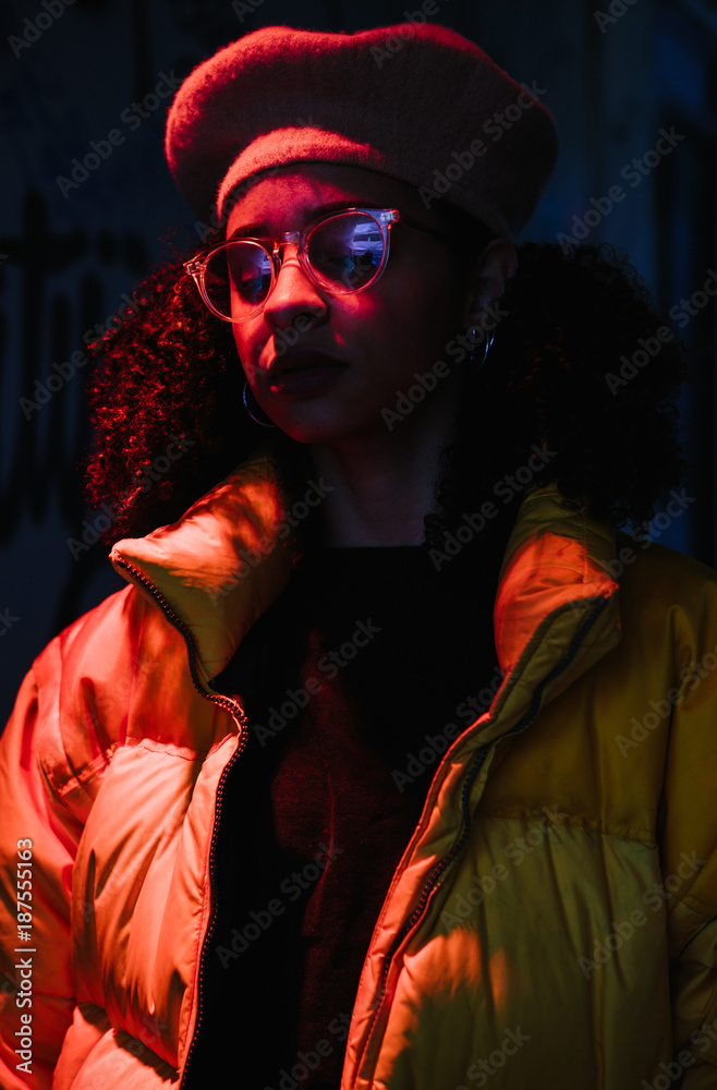 Cool mixed ethnicity woman wearing a puffa jacket standing under an orange spotlight Cool mixed ethnicity woman wearing a puffa jacket standing under an orange spotlight