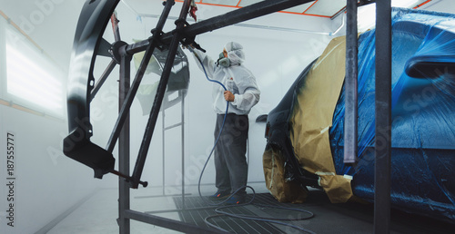 Worker/painter working on car bodywork in paint chamber/workshop.