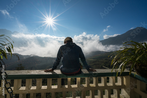 Male tourist sit on balcony seeing mountain landscape with low white clouds under brilliant sky. Ideas for travel and feeling. © Hanoi Photography