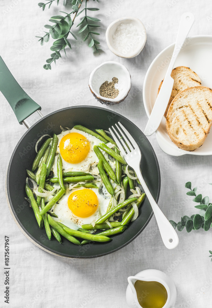 Healthy breakfast or snack - a fried egg with green beans in the pan on a light background, top view