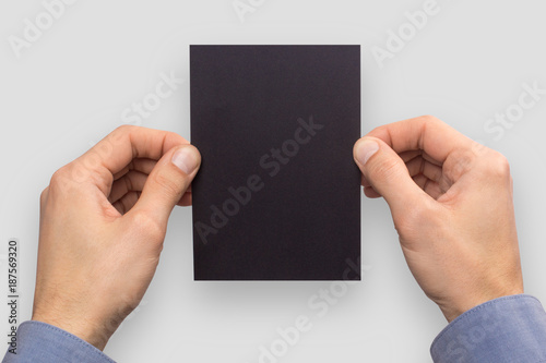 Mockup A6 empty blank black postcard vertically holds the man in his hand in shirt. Isolated on a gray background