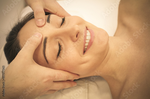 Esthetician massaging head and face of young woman. Close up.