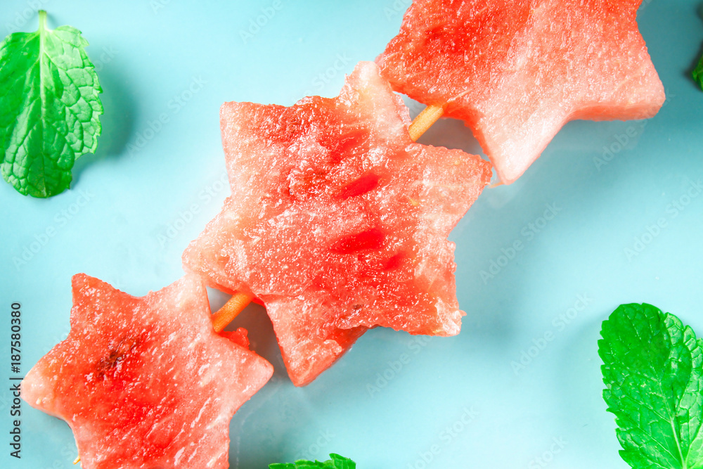 Watermelon in the form of stars on skewers with leaves of mint lies on a blue plate. Top view. Watermelon in the form of stars on skewers with leaves of mint lies on a blue plate. Top view.