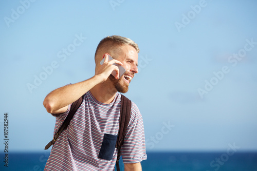 handsome young man laughing and talking on cellphone by the sea