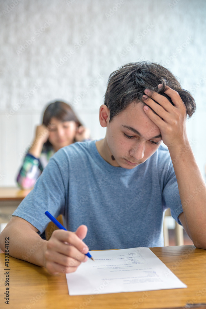 Caucasian male teenager making lesson in the classroom and worried about the test Caucasian male teenager making lesson in the classroom and worried about the test