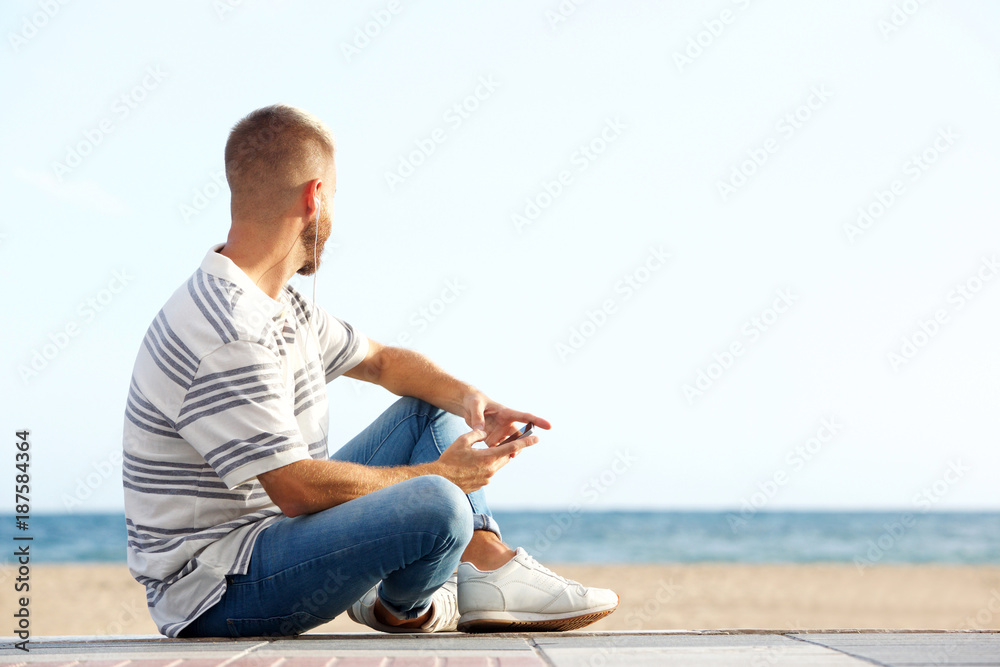 young man sitting by the beach with smart phone and earphones