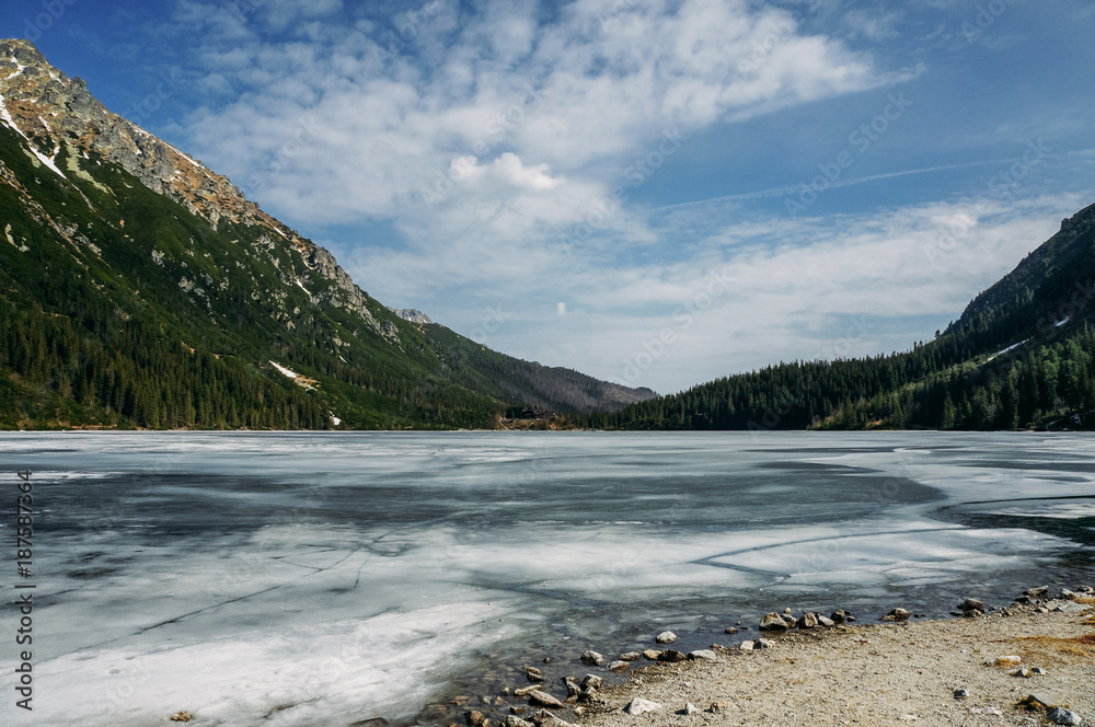 view of lake with ice on surface and mountains on background, Morskie Oko, Sea Eye, Tatra National Park, Poland