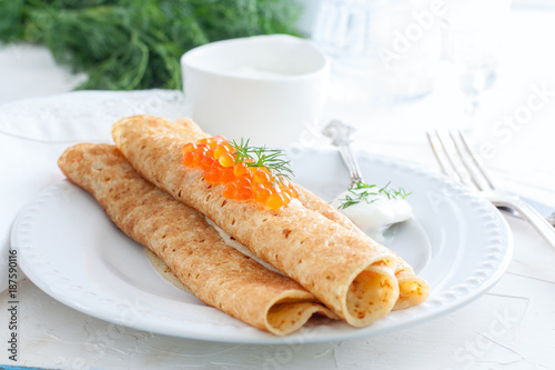 Homemade pancakes with red caviar and fresh herbs on a white plate, horizontal