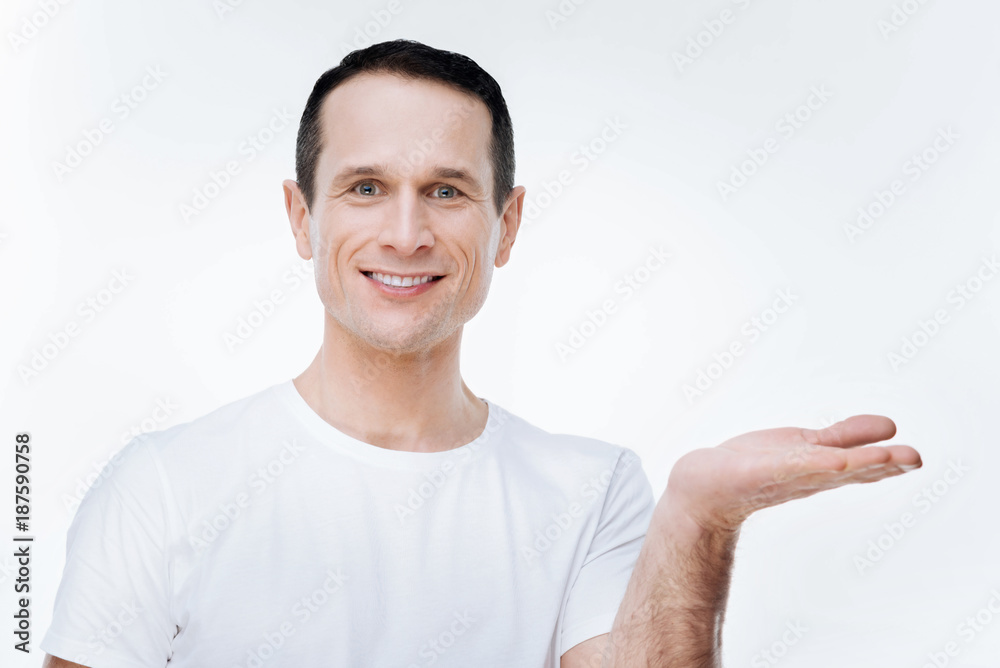 Positive mood. Cheerful nice delighted man smiling and looking at you while holding his hand Positive mood. Cheerful nice delighted man smiling and looking at you while holding his hand