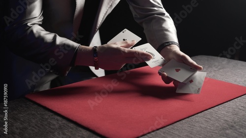 A magician makes a magic trick and reveals 4 aces over a red carpet during a show in a casino