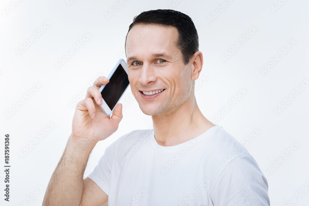 Phone call. Joyful nice pleasant man holding his smartphone and looking at  you while making a phone call Photos | Adobe Stock
