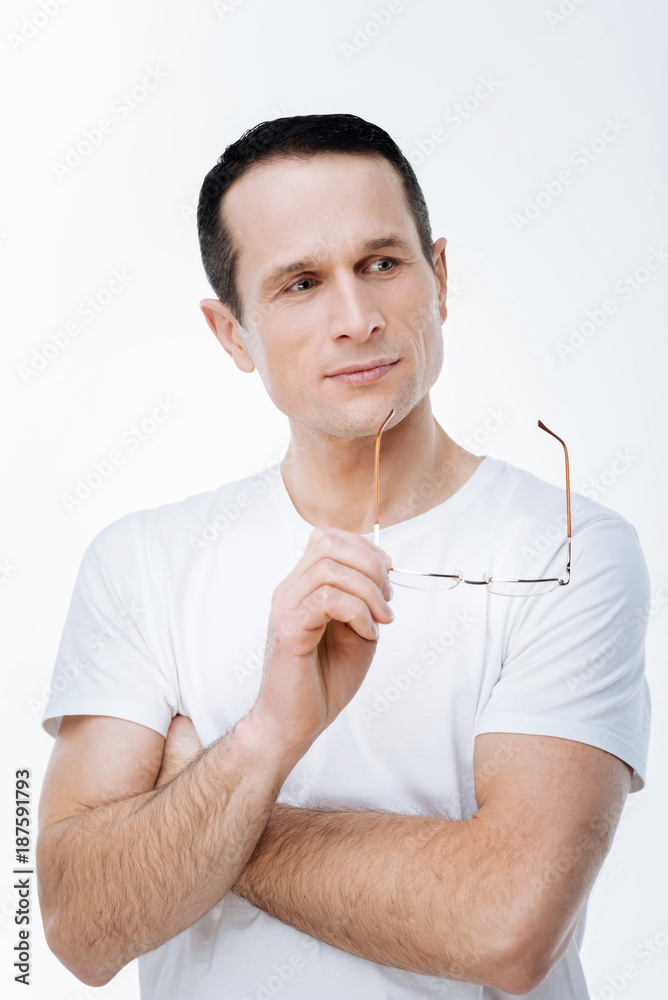 Tough problem. Nice positive smart man holding his glasses and thinking about the problem while looking for a solution to it Tough problem. Nice positive smart man holding his glasses and thinking about the problem while looking for a solution to it