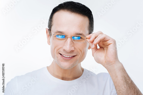 Bad eyesight. Happy positive joyful man smiling and fixing his glasses while looking at you