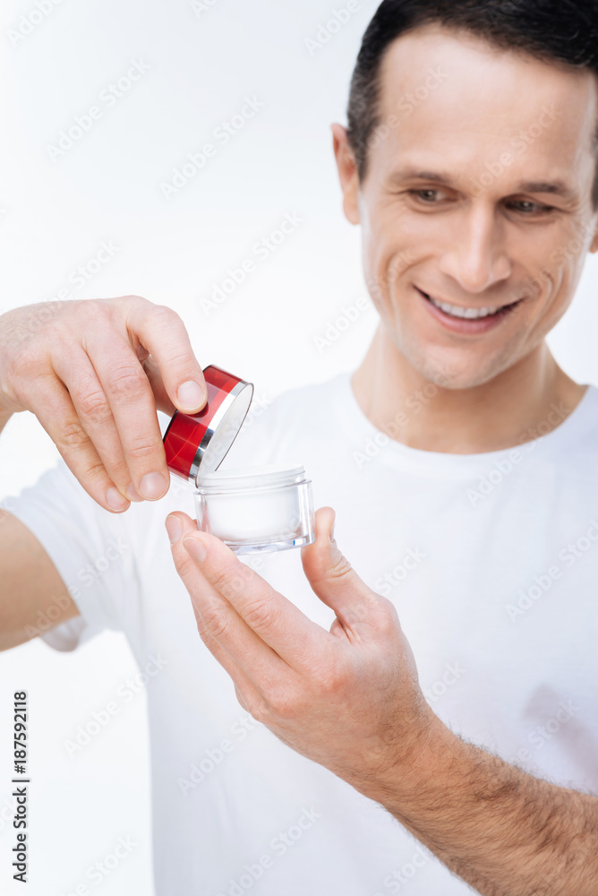 Facial care. Selective focus of a bottle of a facial cream being opened by a pleasant nice handsome man Facial care. Selective focus of a bottle of a facial cream being opened by a pleasant nice handsome man