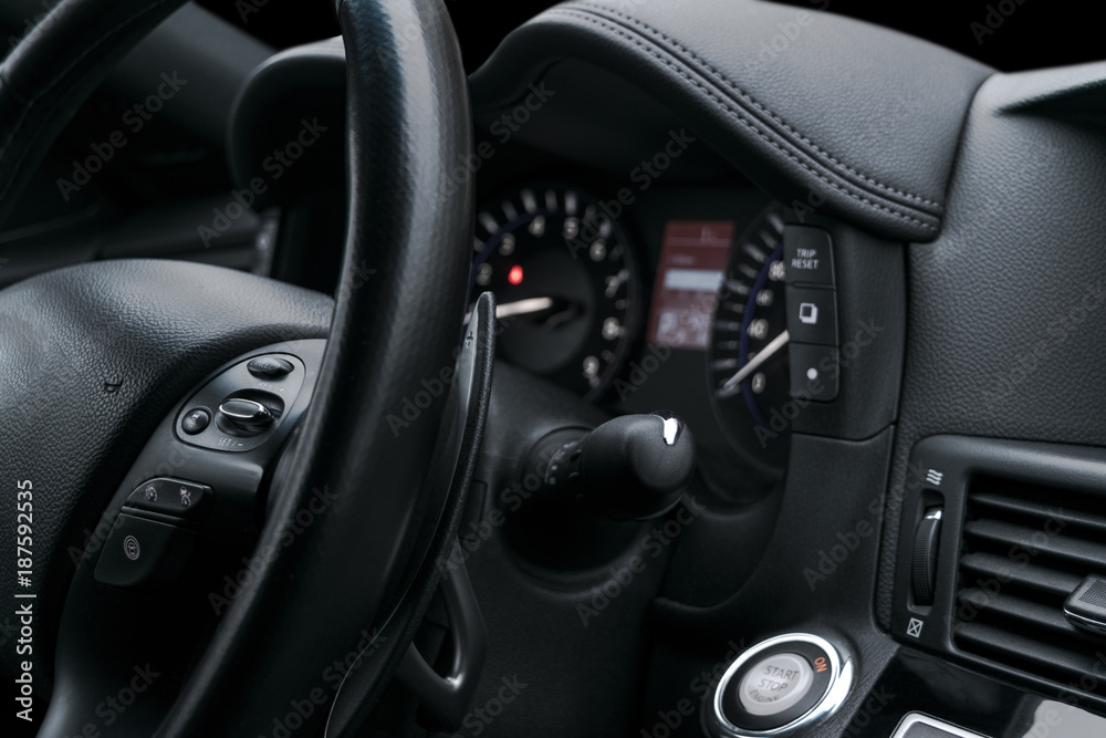 Cruise control buttons on the steering wheel of a modern car with black perforated leather interior. Modern car interior details.