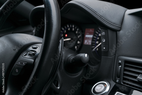 Cruise control buttons on the steering wheel of a modern car with black perforated leather interior. Modern car interior details. © Aleksei