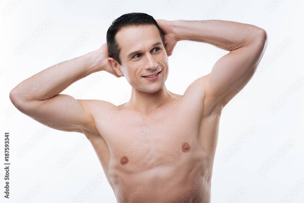 Sporty figure. Positive nice athletic man smiling and looking aside while holding hands behind his head Sporty figure. Positive nice athletic man smiling and looking aside while holding hands behind his head