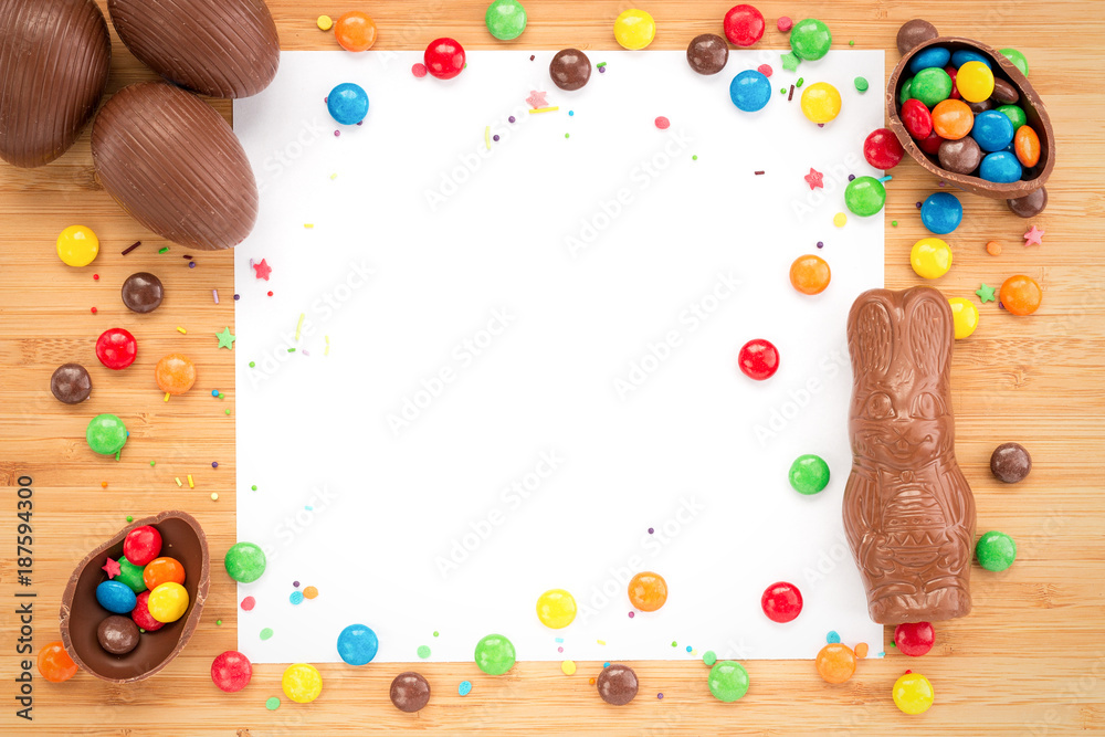 Obraz premium Easter concept painted and chocolate eggs, sweets, drops, candys for holiday with place for text pattern on wooden light background with paper