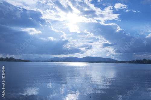 A blue lake with bright sunshine and a blue sky with white clouds.