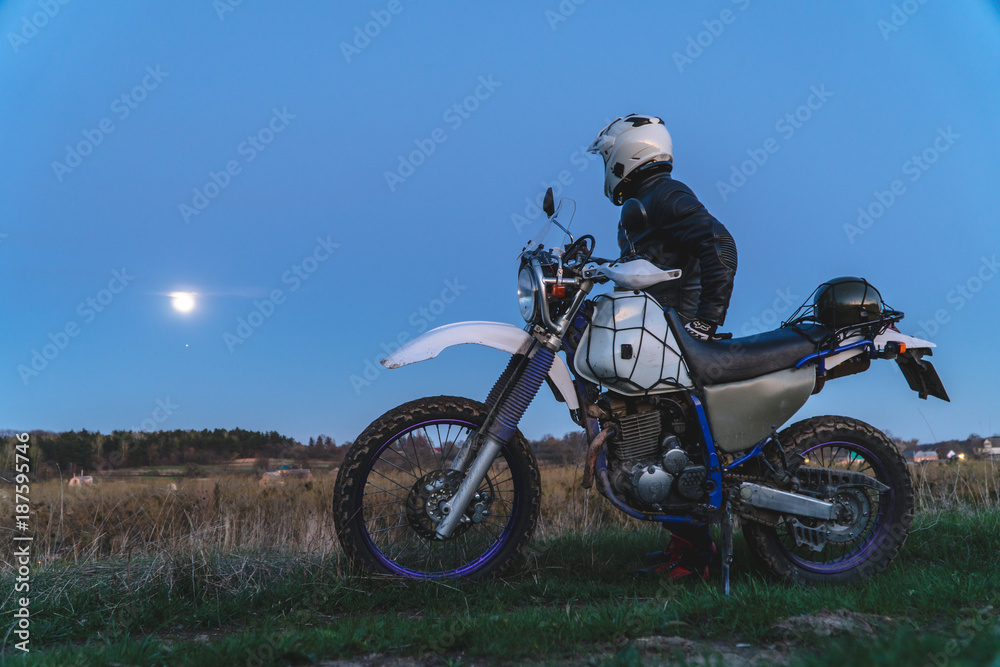 Active way of life, enduro motorcycle, a guy looks at the stars at night and the moon, unity with nature, the spirit of adventure, escape from the hustle and bustle of the city, travel concept